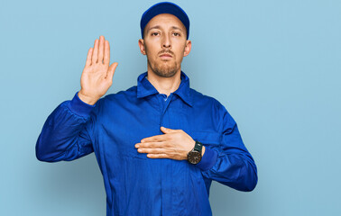 Bald man with beard wearing builder jumpsuit uniform swearing with hand on chest and open palm,...