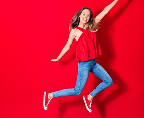 Young beautiful woman wearing casual clothes smiling happy. Jumping with smile on face and arms opened over isolated red background