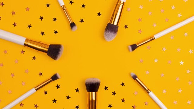 Stop motion animation of gold colored  cosmetics white brushes set for makeup and stars on bright yellow background. Cosmetics and beauty concept template Make up concept with copy space flat lay