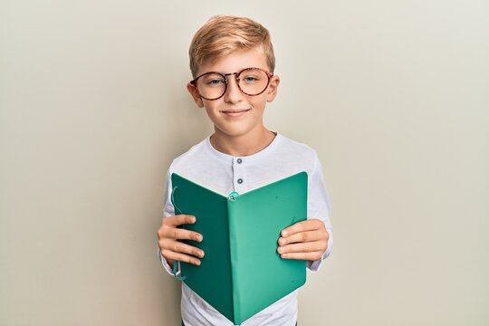 Little caucasian boy kid reading a book wearing glasses relaxed with serious expression on face. simple and natural looking at the camera.