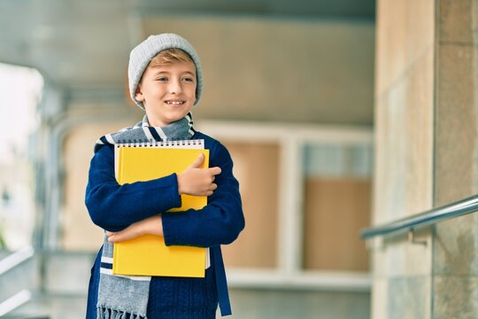 Adorable blond student kid smiling happy holding book at the school.