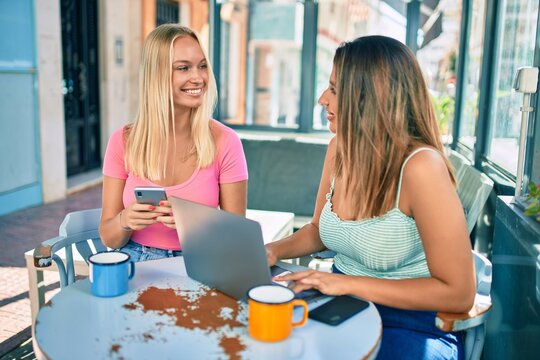 Two beautiful and young girl friends meeting at cafeteria using laptop and smartphone