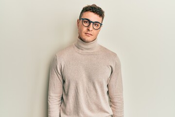Hispanic young man wearing casual turtleneck sweater relaxed with serious expression on face. simple and natural looking at the camera.