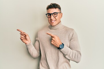 Hispanic young man wearing casual turtleneck sweater pointing aside worried and nervous with both...