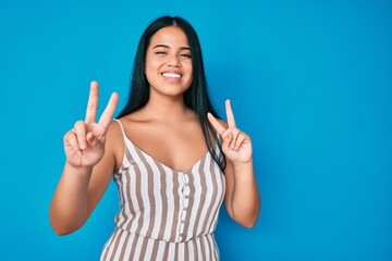 Young beautiful asian girl wearing casual clothes smiling looking to the camera showing fingers doing victory sign. number two.