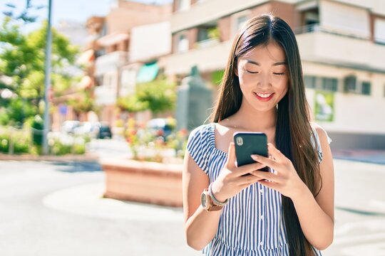 Young chinese woman smiling happy using smartphone at street of city.