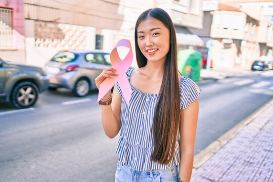 Young chinese woman smiling happy holding pink ribbon at street of city.