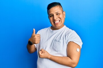 Young latin man using glucose meter button smiling happy and positive, thumb up doing excellent and approval sign