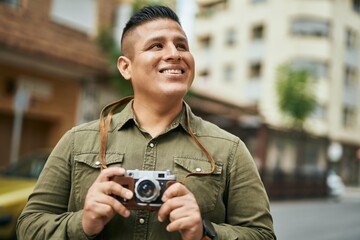 Young latin tourist man smiling happy using vintage camera at the city.