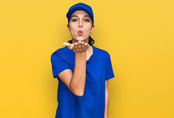Young hispanic girl wearing delivery courier uniform looking at the camera blowing a kiss with hand on air being lovely and sexy. love expression.