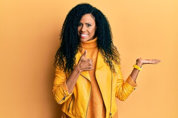Middle age african american woman wearing wool winter sweater and leather jacket showing palm hand and doing ok gesture with thumbs up, smiling happy and cheerful