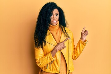 Middle age african american woman wearing wool winter sweater and leather jacket pointing aside worried and nervous with both hands, concerned and surprised expression