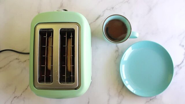 Woman takes toast from the toaster and puts it on a plate on table with black coffee