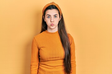 Young brunette teenager wearing casual yellow sweater puffing cheeks with funny face. mouth...