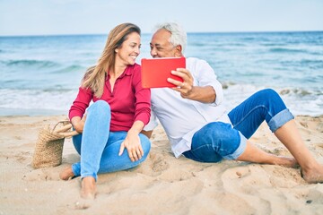 Fototapeta premium Middle age hispanic couple smiling happy making selfie by the tablet at the beach.