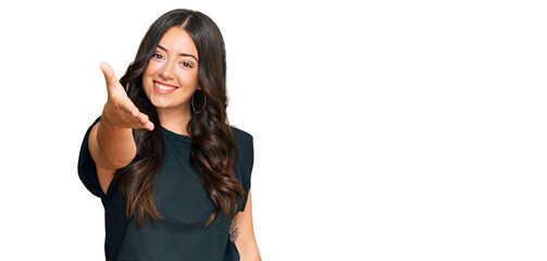 Obraz premium Beautiful brunette young woman wearing black shirt smiling friendly offering handshake as greeting and welcoming. successful business.