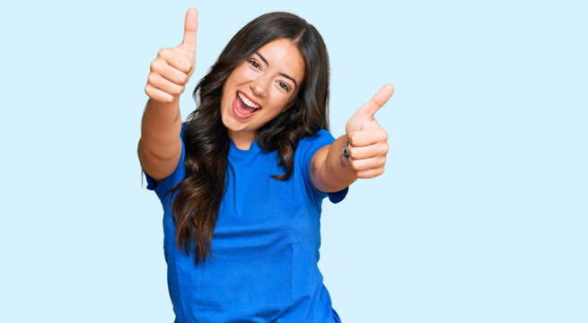 Beautiful brunette young woman wearing casual clothes approving doing positive gesture with hand, thumbs up smiling and happy for success. winner gesture.