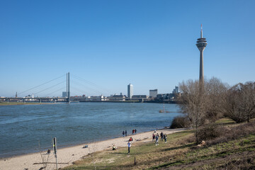 View of people enjoy outdoor activities on the beach at waterside along Rhine river with background of suspension bridges and cityscape of Düsseldorf.