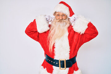 Old senior man with grey hair and long beard wearing santa claus costume with suspenders covering ears with fingers with annoyed expression for the noise of loud music. deaf concept.