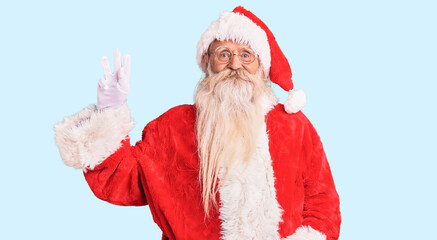 Old senior man with grey hair and long beard wearing traditional santa claus costume showing and pointing up with fingers number three while smiling confident and happy.
