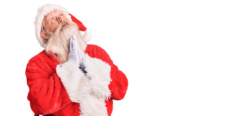 Old senior man with grey hair and long beard wearing traditional santa claus costume begging and praying with hands together with hope expression on face very emotional and worried. begging.