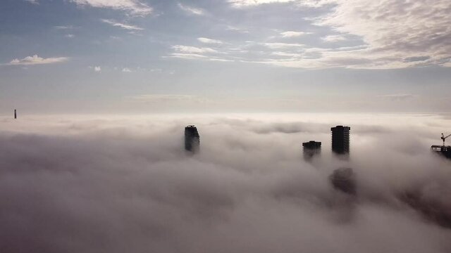 2.7K aerial flight over dense fog with 5 skycrapers peaking their tops through the fog
