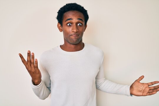 African handsome man wearing casual winter sweater clueless and confused expression with arms and hands raised. doubt concept.