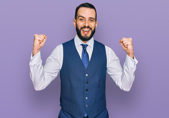 Young man with beard wearing business vest celebrating surprised and amazed for success with arms raised and open eyes. winner concept.