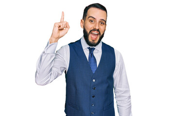 Young man with beard wearing business vest pointing finger up with successful idea. exited and happy. number one.