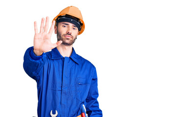 Young hispanic man wearing worker uniform doing stop sing with palm of the hand. warning expression with negative and serious gesture on the face.