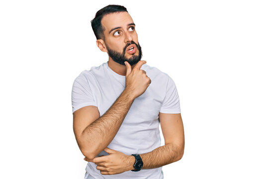 Young man with beard wearing casual white t shirt thinking worried about a question, concerned and nervous with hand on chin