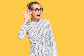 Beautiful blonde woman wearing business shirt and glasses smiling with hand over ear listening an hearing to rumor or gossip. deafness concept.