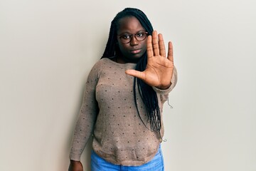 Young black woman with braids wearing casual clothes and glasses doing stop sing with palm of the...