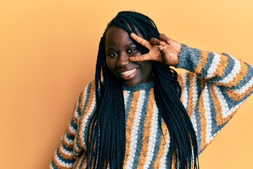 Young black woman with braids wearing casual winter sweater doing peace symbol with fingers over face, smiling cheerful showing victory