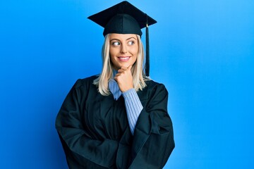 Beautiful blonde woman wearing graduation cap and ceremony robe with hand on chin thinking about question, pensive expression. smiling with thoughtful face. doubt concept.