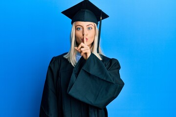 Beautiful blonde woman wearing graduation cap and ceremony robe asking to be quiet with finger on lips. silence and secret concept.