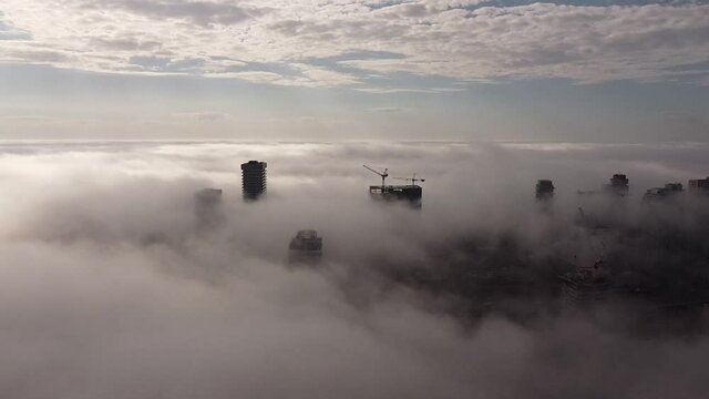 2.7K aerial flight over dense moving fog with buildings popping through the fog and a view of cars flying by on the Gardiner Expressway below