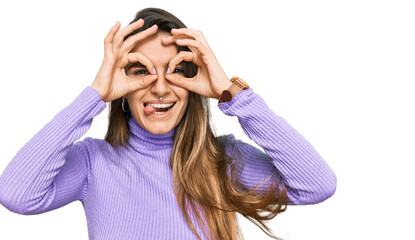 Young hispanic woman wearing casual clothes doing ok gesture like binoculars sticking tongue out, eyes looking through fingers. crazy expression.