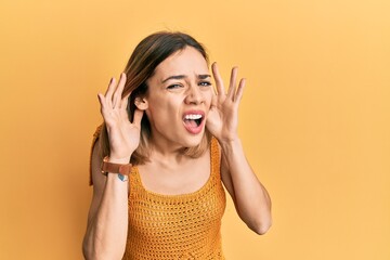 Fototapeta premium Young caucasian blonde woman wearing casual yellow t shirt trying to hear both hands on ear gesture, curious for gossip. hearing problem, deaf