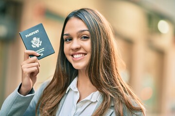 Young latin businesswoman smiling happy holding united states passport at the city.