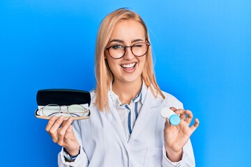 Beautiful caucasian oculist woman holding glasses and contact lenses winking looking at the camera...