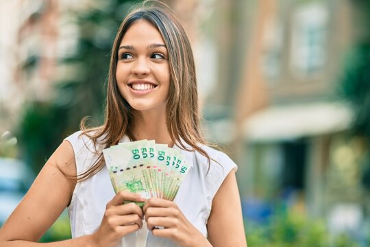 Beautiful latin teenager girl smiling happy holding hong kong dollars at the city.
