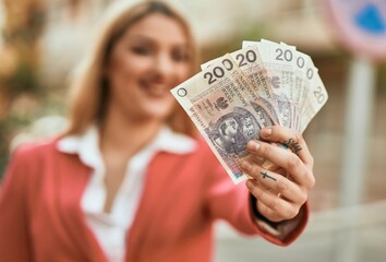 Young blonde businesswoman smiling happy holding polish zloty at the city.