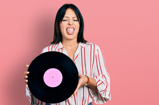 Young hispanic girl holding vinyl disc sticking tongue out happy with funny expression.