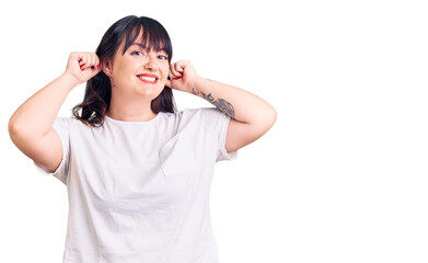 Young plus size woman wearing casual clothes smiling pulling ears with fingers, funny gesture....