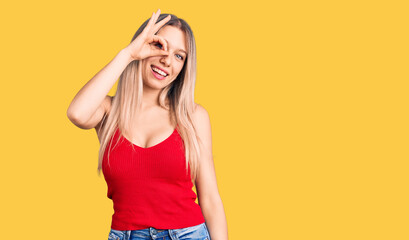 Obraz na płótnie Canvas Young beautiful blonde woman wearing casual clothes smiling happy doing ok sign with hand on eye looking through fingers
