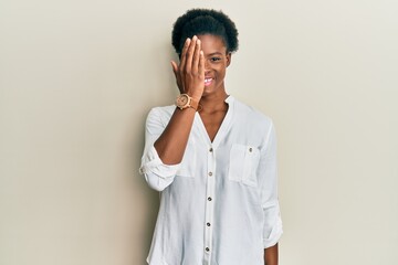 Young african american girl wearing casual clothes covering one eye with hand, confident smile on face and surprise emotion.