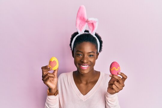 Young african american girl wearing cute easter bunny ears holding painted eggs smiling with a happy and cool smile on face. showing teeth.