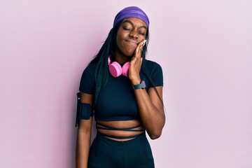 Young african american woman wearing gym clothes and using headphones touching mouth with hand with painful expression because of toothache or dental illness on teeth. dentist