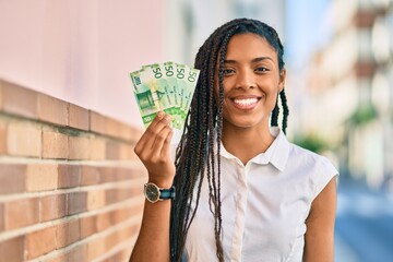 Young african american woman smiling happy holding norwegian 50 krona banknotes at the city.